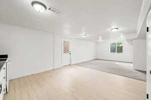 Basement featuring a textured ceiling, baseboards, light wood-type flooring, and visible vents