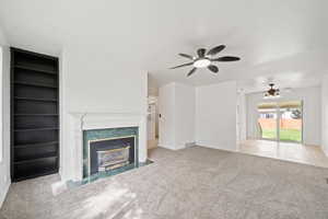 Unfurnished living room featuring carpet, a premium fireplace, baseboards, ceiling fan, and built in shelves