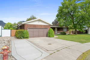Ranch-style house featuring a front lawn, driveway, an attached garage, and fence