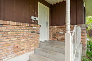 Entrance to property featuring covered porch and brick siding