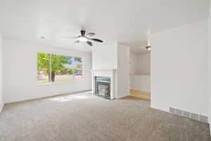 Unfurnished living room with a premium fireplace, ceiling fan, visible vents, and carpet floors