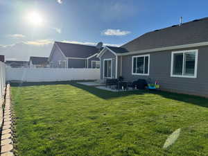Rear view of house featuring entry steps, a patio, a yard, and a fenced backyard
