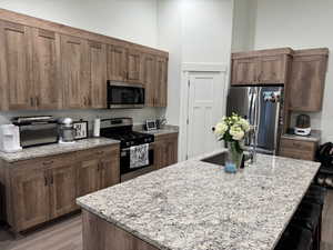 Kitchen featuring light stone counters, a breakfast bar, an island with sink, light wood-style flooring, and stainless steel appliances