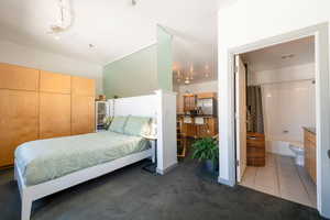 Carpeted bedroom with tile patterned flooring, connected bathroom, stainless steel refrigerator with ice dispenser, and visible vents