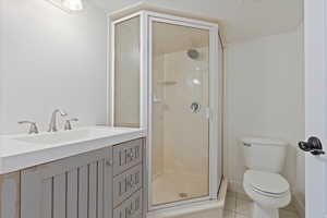 Bathroom with a stall shower, toilet, baseboards, tile patterned flooring, and vanity