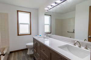Full bath with a sink, toilet, double vanity, and wood finished floors