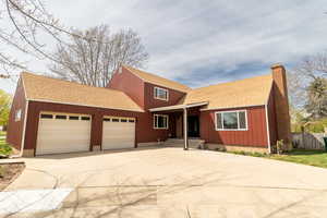 Traditional home with a shingled roof, a chimney, a garage, and concrete driveway