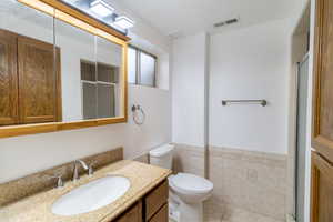 Full bath with visible vents, a wainscoted wall, toilet, tile walls, and a stall shower