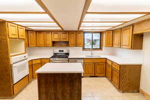 Kitchen with brown cabinetry, a kitchen island, a sink, and appliances with stainless steel finishes