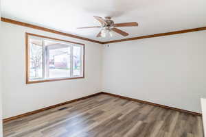 Spare room featuring light wood-type flooring, crown molding, a ceiling fan, and baseboards