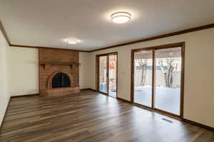 Unfurnished living room with a textured ceiling, ornamental molding, visible vents, dark wood-style flooring, and baseboards
