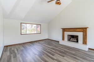Unfurnished living room with a ceiling fan, a tile fireplace, wood finished floors, and vaulted ceiling
