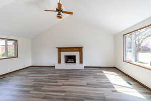 Unfurnished living room featuring a ceiling fan, a fireplace with raised hearth, visible vents, wood finished floors, and baseboards