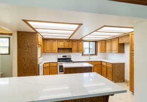 Kitchen with stainless steel range with gas cooktop, brown cabinetry, a kitchen island, light countertops, and a sink