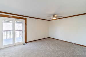 Spare room featuring baseboards, crown molding, visible vents, ceiling fan, and carpet