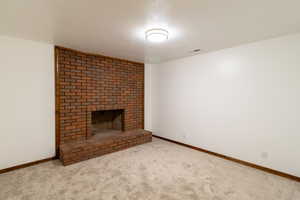 Unfurnished living room with a fireplace, a textured ceiling, visible vents, carpet floors, and baseboards