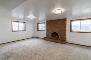 Unfurnished living room featuring baseboards, carpet, a brick fireplace, and a textured ceiling