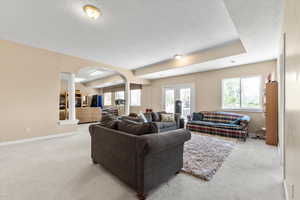 Carpeted living room featuring arched walkways, baseboards, and a textured ceiling