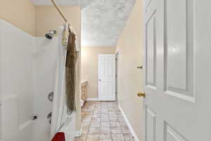Bathroom with vanity, a textured ceiling, stone finish floor, baseboards, and shower / tub combo