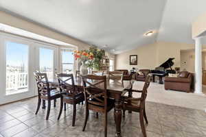 Carpeted dining room featuring tile patterned floors, visible vents, lofted ceiling, and ornate columns