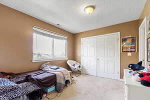 Bedroom featuring light colored carpet, a closet, a textured ceiling, and visible vents