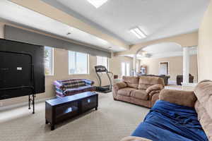 Carpeted living room featuring arched walkways, baseboards, and decorative columns