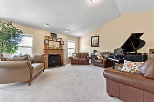 Living area featuring a wealth of natural light, light carpet, a fireplace with flush hearth, and vaulted ceiling
