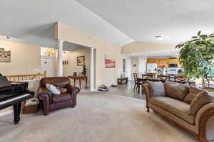 Living room featuring lofted ceiling, light carpet, ornate columns, and baseboards