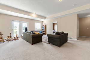 Living area featuring french doors, a textured ceiling, visible vents, baseboards, and light carpet