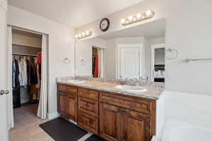 Bathroom with a tub, double vanity, a walk in closet, and a sink