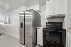 Kitchen with stainless steel refrigerator with ice dispenser, under cabinet range hood, black range with electric stovetop, white cabinets, and baseboards