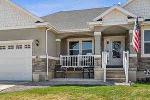 Entrance to property with a porch, roof with shingles, a garage, and stone siding