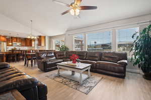 Living room with visible vents, light wood-style flooring, lofted ceiling, and ceiling fan with notable chandelier