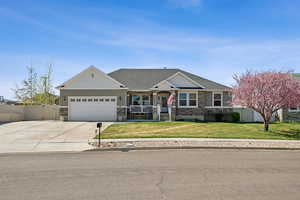 View of front of property featuring a porch, fence, stone siding, a garage, and a front lawn