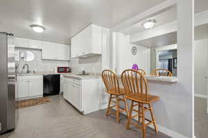 Kitchen featuring freestanding refrigerator, white cabinetry, black dishwasher, and a sink