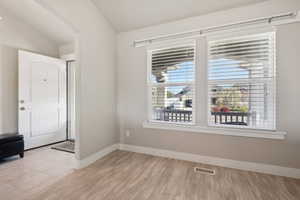 Spare room with light wood-type flooring, visible vents, baseboards, arched walkways, and lofted ceiling