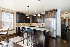 Kitchen featuring stainless steel appliances, a breakfast bar, dark wood finish cabinetry, pendant lighting, and light stone counters