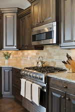 Kitchen with stainless steel appliances, dark wood finish cabinets, light stone countertops, and tasteful backsplash
