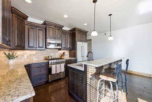 Kitchen featuring dark wood finish cabinets, decorative light fixtures, high end appliances, and dark wood finished floors