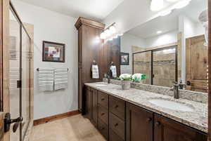 Bathroom with double vanity, a shower stall, and stone tile floors