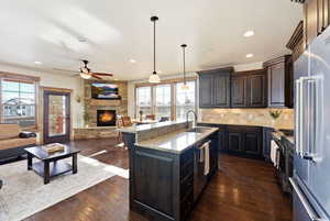Kitchen with open floor plan, dark wood finish cabinets, stainless steel appliances, light stone countertops, and decorative light fixtures