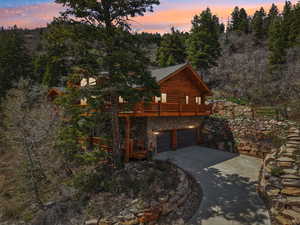 View of front of home featuring a deck, a garage, log exterior, concrete driveway, and stone siding