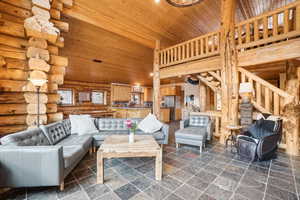 Living area with rustic walls, stone tile floors, wood ceiling, and a towering ceiling
