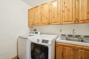 Clothes washing area with cabinet space, washer and clothes dryer, a sink, and a textured wall