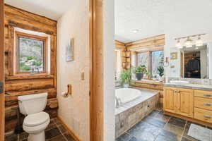 Full bath with a garden tub, toilet, log walls, and a textured wall