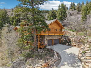 View of side of home featuring log siding, a deck, an attached garage, stone siding, and concrete driveway