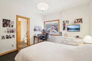Bedroom with connected bathroom, baseboards, and dark wood finished floors