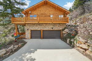 View of front of property with stone siding, concrete driveway, log exterior, and a garage