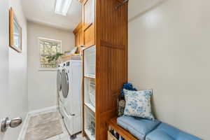 Washroom featuring baseboards, washing machine and dryer, light tile patterned floors, and cabinet space