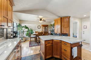 Kitchen with a ceiling fan, lofted ceiling, light stone counters, and a center island